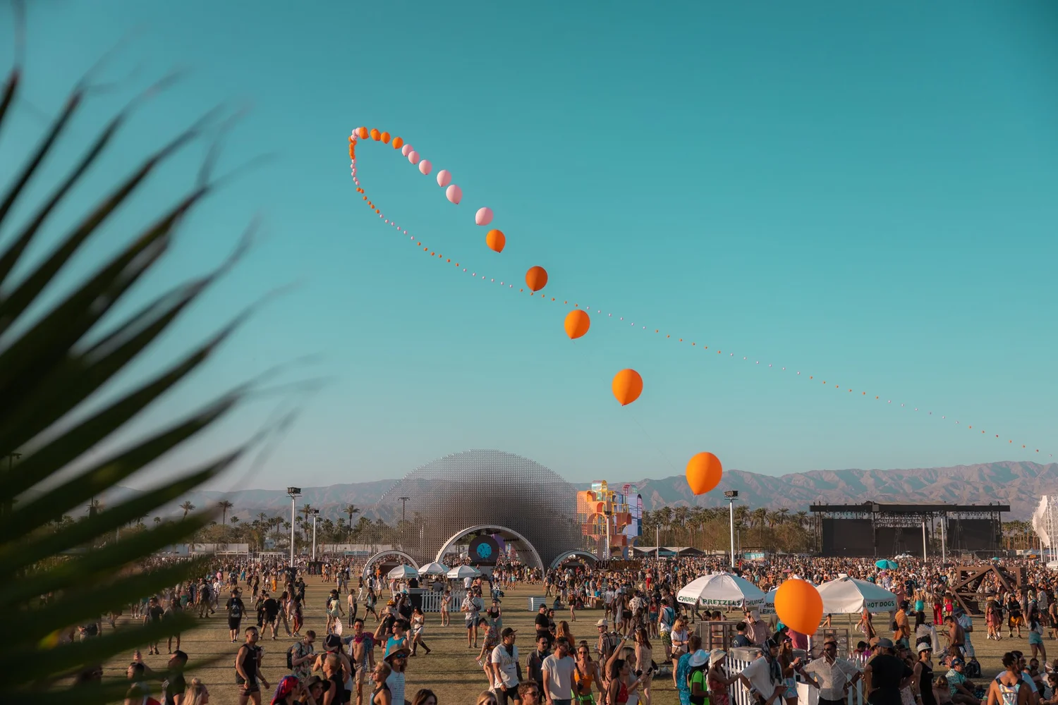 Coachella festival grounds at golden hour with balloon chains floating against a turquoise sky