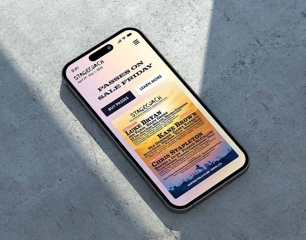 iPhone on concrete showing Stagecoach mobile homepage with passes on sale hero and lineup poster